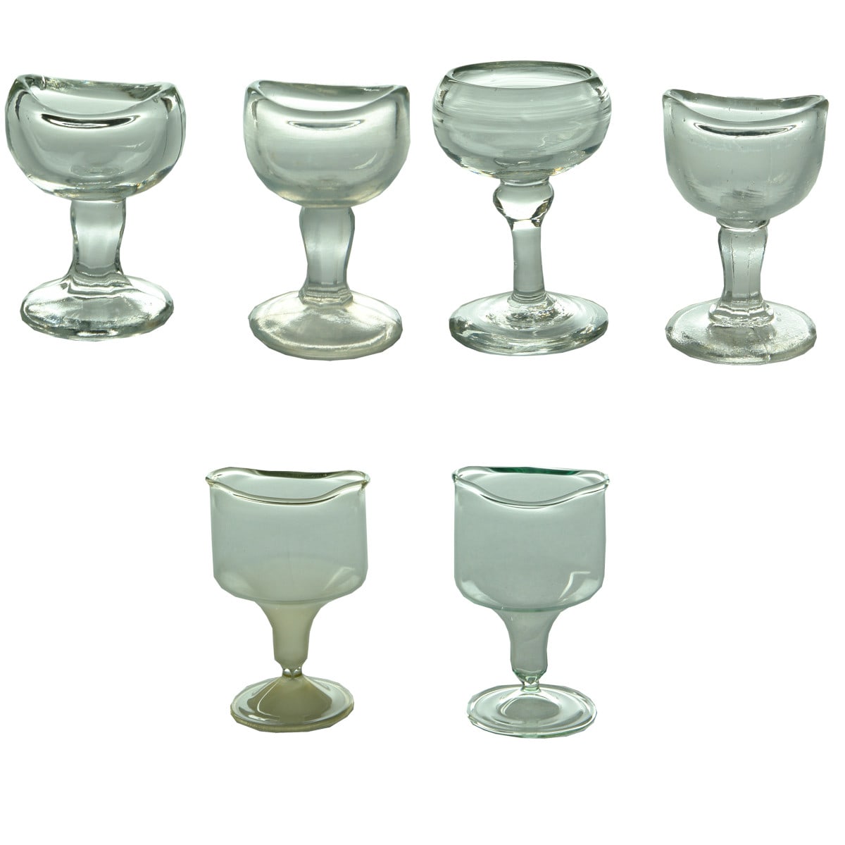 6 Eye Baths: Four clear glass pedestal type Eye Baths and Two "Freeblown" Eyebaths.