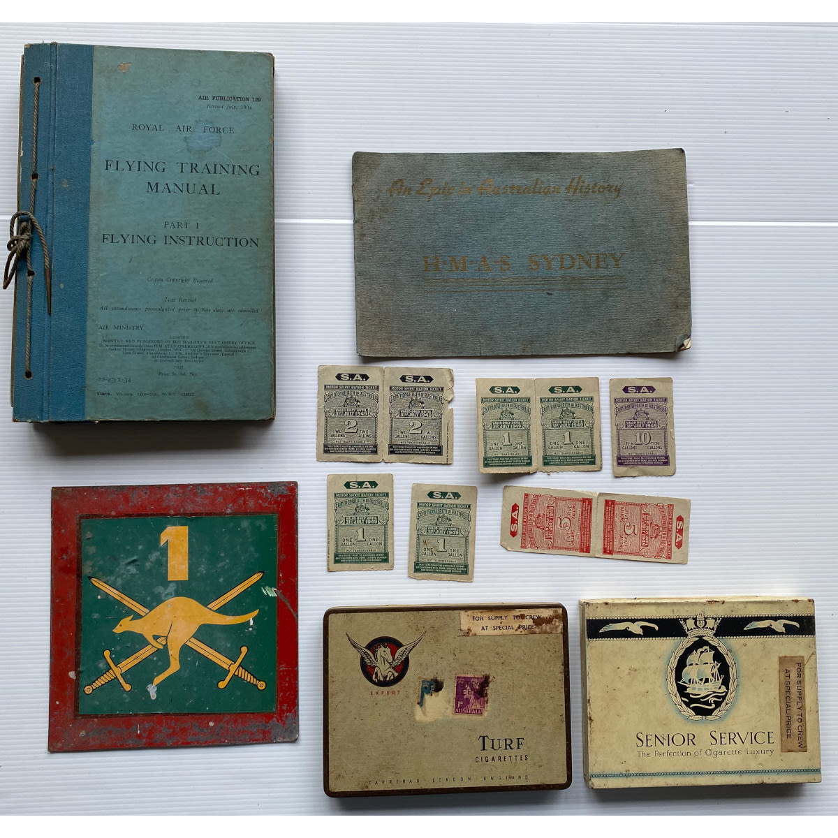 Group Military/War related items: Royal Air Force Flying Manual 1934 HMAS Sydney pamphlet 2 cigarette tins for crew only Tin vehicle ID 9 SA petrol ration tickets.