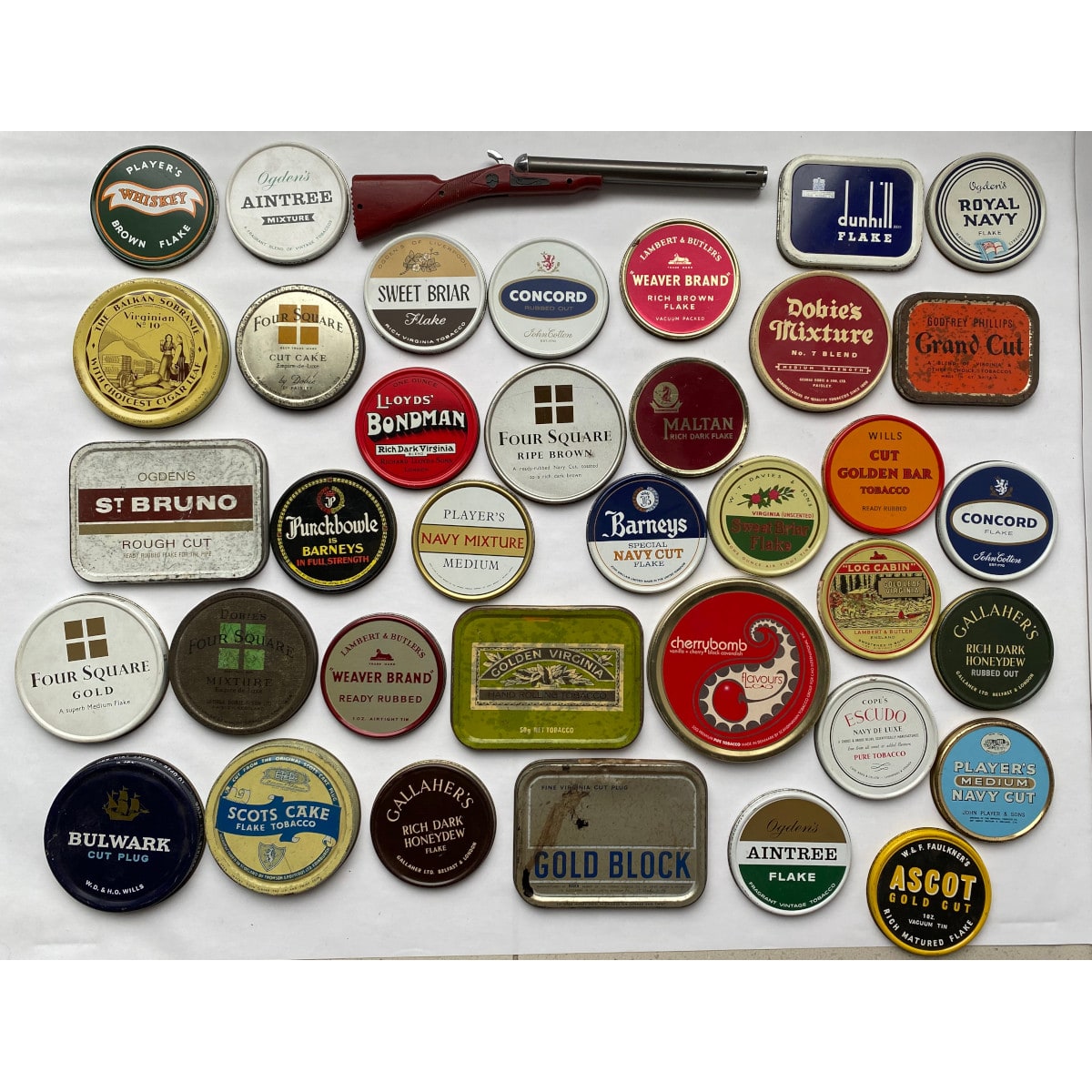 Tobacciana: 35 Tobacco Tin Lids and a long Lighter in the shape of a double barrelled shotgun.