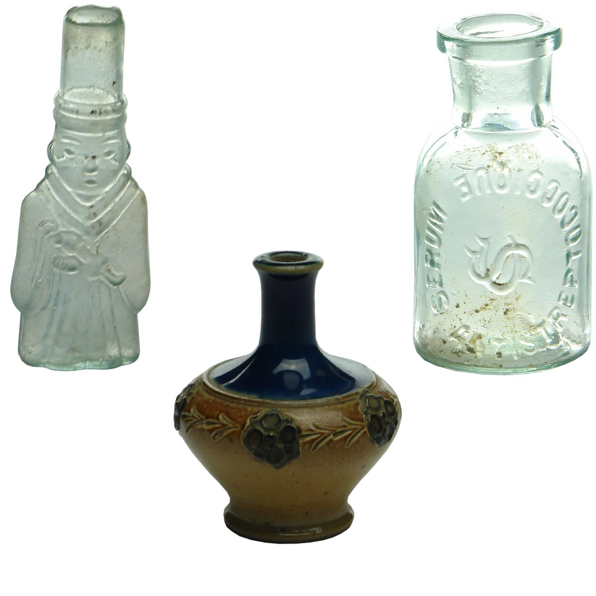 3 Tiny bottles/items: 1. Figural shear lip bottle. Man in robe holding a scroll or something. Confucious? 75 mm. 2. Serum Antistreptococcique. 50 mm. 3. Royal Doulton sample. Salt Glaze with blue top. Flowers around sides. 64 mm.