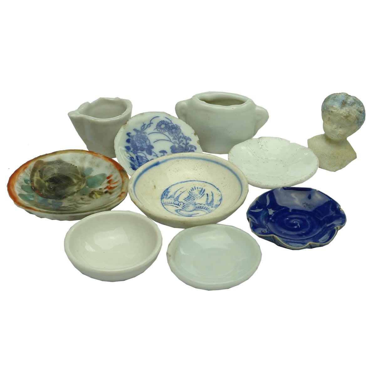 Dolls. Range of doll set pieces including seven small plates, two little white jugs of sorts and a small doll's head.