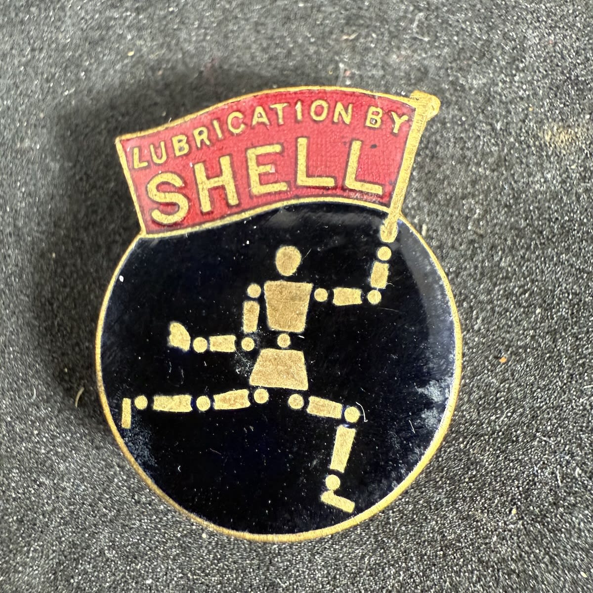 Enamel Badge. Shell Stickman holding a flag - Lubrication by Shell. Fattorini & Sons Ltd Bradford Works Birmingham.
