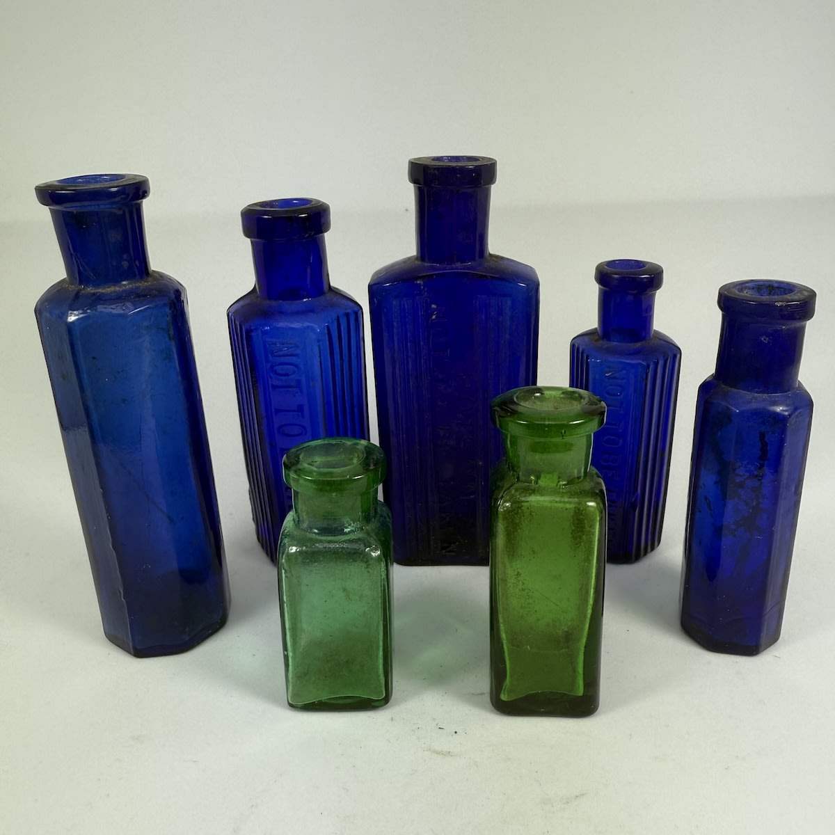 7 Small Bottles: 5 Blue Poisons/Vials, Not to be taken and more; 2 small square Green bottles.