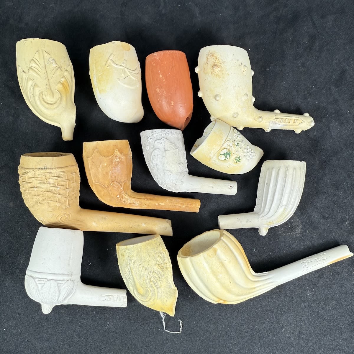 12 Decorated clay pipe bowls. Various patterns and one terracotta with a small stamp.