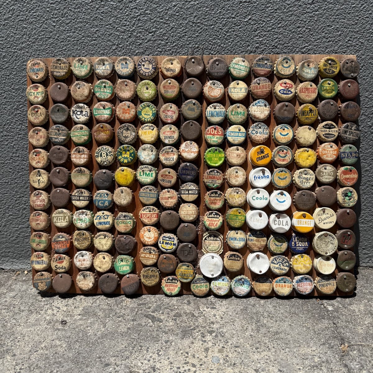 Board with mostly crown seal caps nailed on. Tarax, Franklins, Marchants, Mosley, Joes, Cohns, McCabes, Cottees and many more. Around 150 or so.