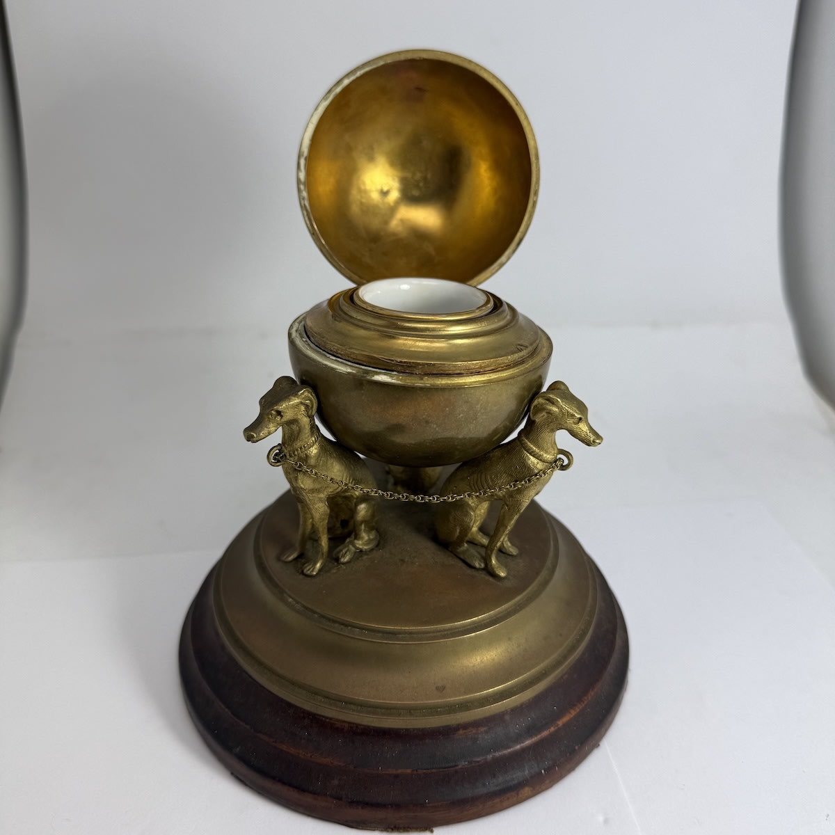 Inkwell. Brass inkwell with three whippet dogs. Chain between them around their necks. Dogs are holding a globe with a brass insert and porcelain inkwell. Wooden stand with leather on the base. Brass insert and inner of the bottom of the globe have IIIIXXXX hand scratched into them.