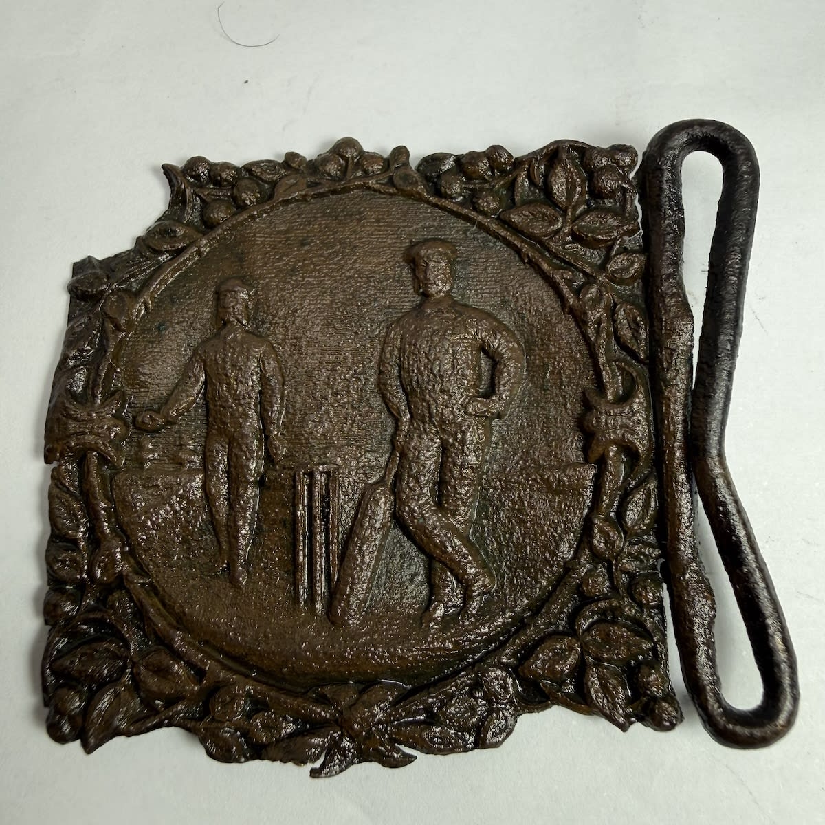 Cricket Belt Buckle. Batsman leaning on his bat in front of the stumps. Bowler behind him with ball in his outstretched hand.