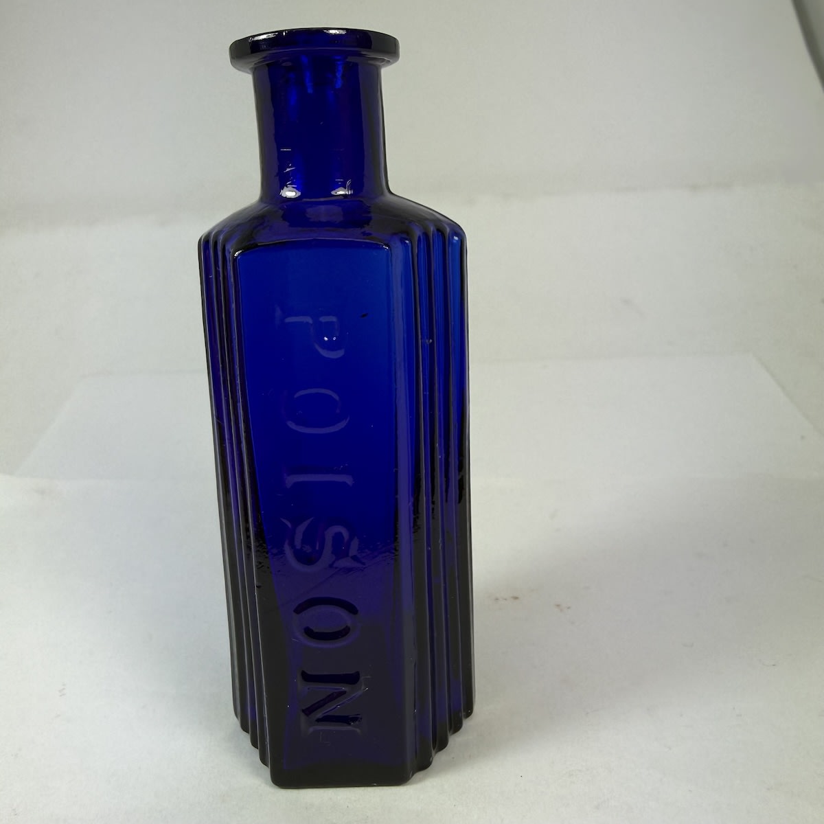 Poison. Hexagonal with deep vertical grooves to the panels either side of the embossed panel. Cobalt Blue. 1 oz. 94 mm.