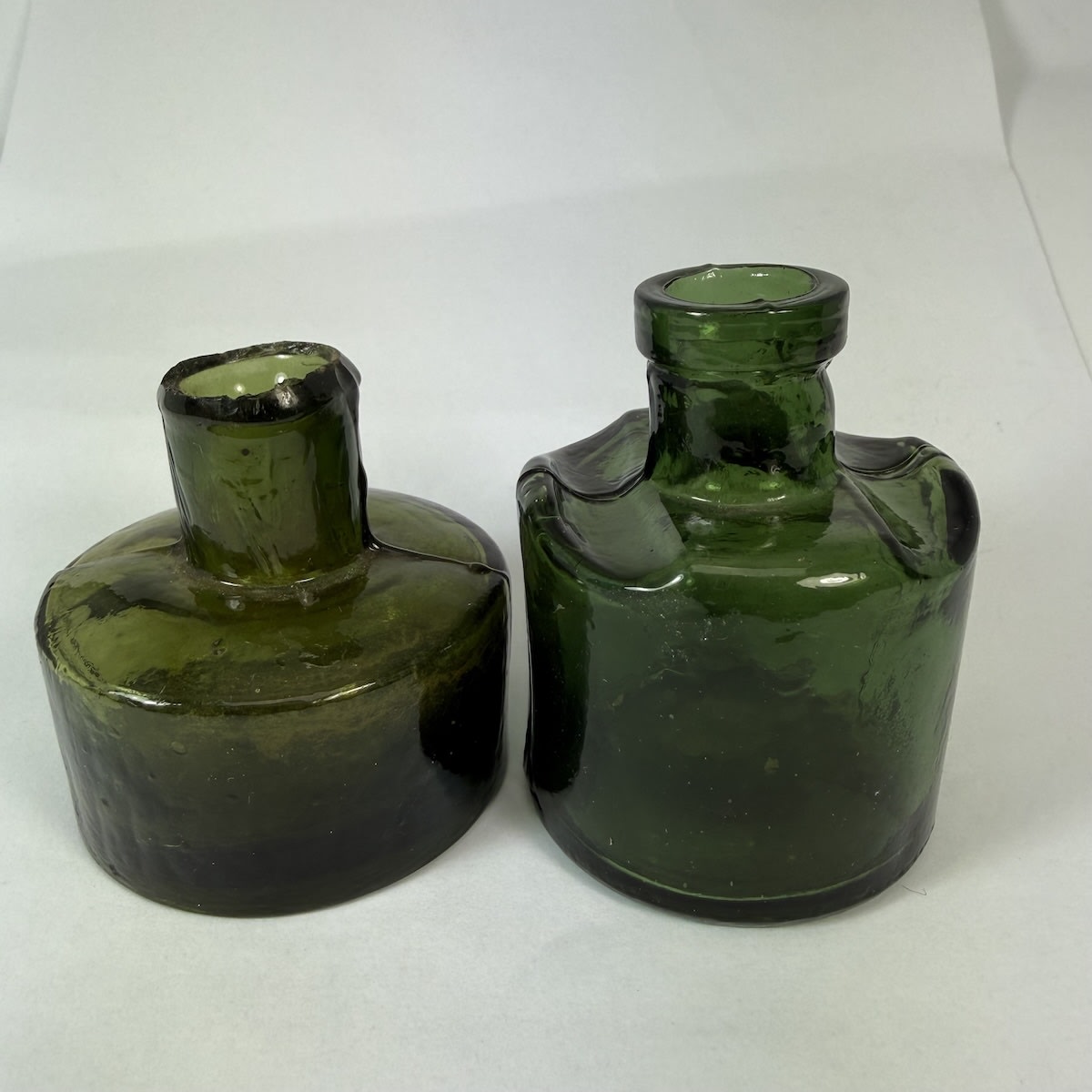2 Green Glass inks: Squat round one with shear lip; Round with crude machine finished lip and two grooves for pen rests on the shoulder.