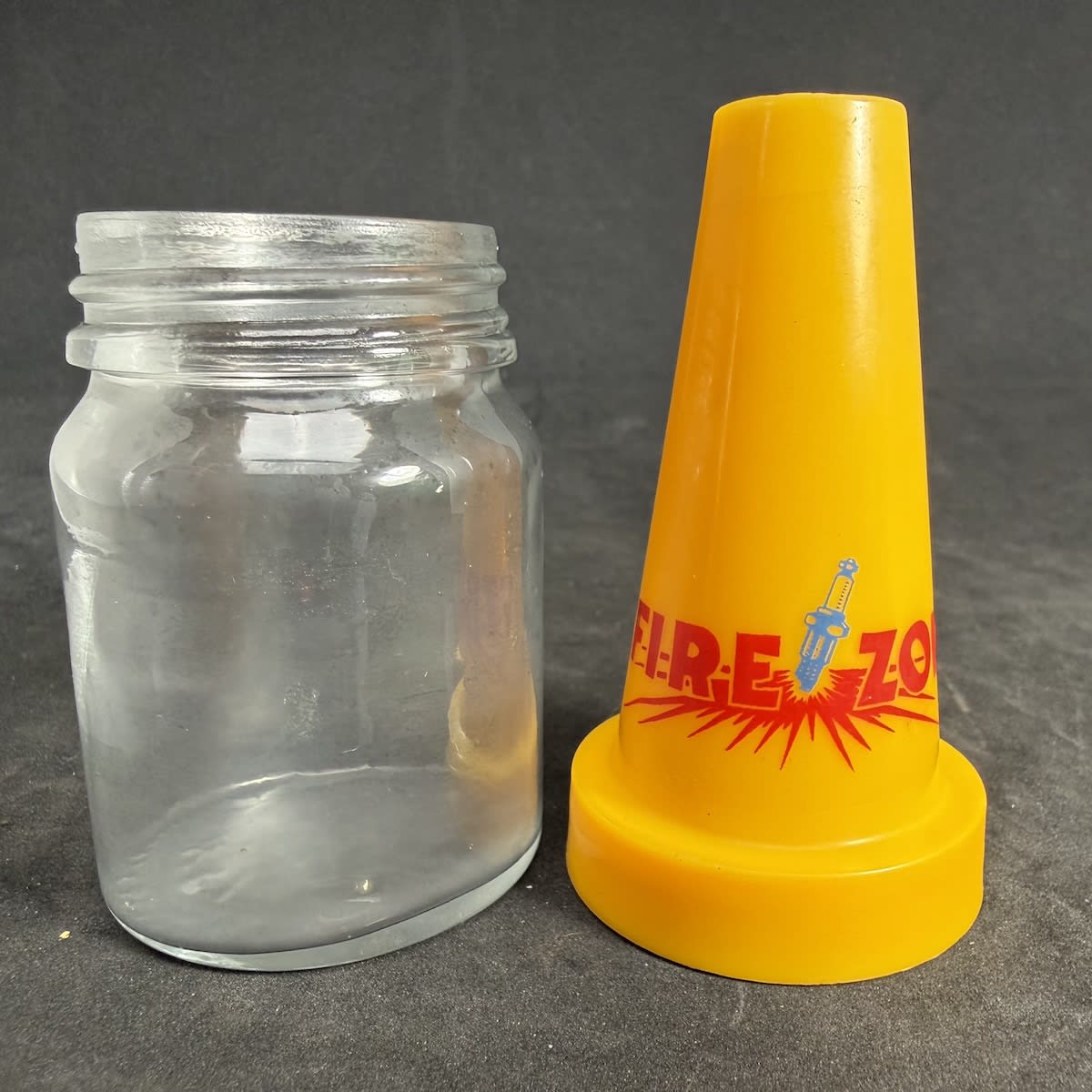 Plastic pourer on small glass jar. Firezone. Sparkplug. Base of jar is Modern AGM Monogram ISM 902.