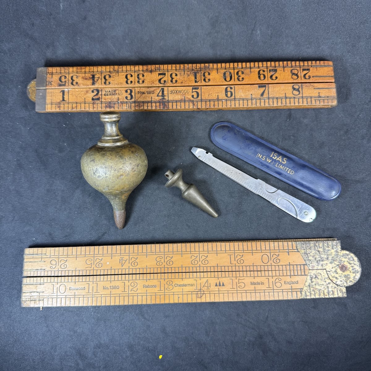 5 Measuring Items/Tools: 2 x fold out wooden rulers; ISAS NSW Ltd Multi tool in plastic case; Plumb bobs, one larger very heavy one, both brass.