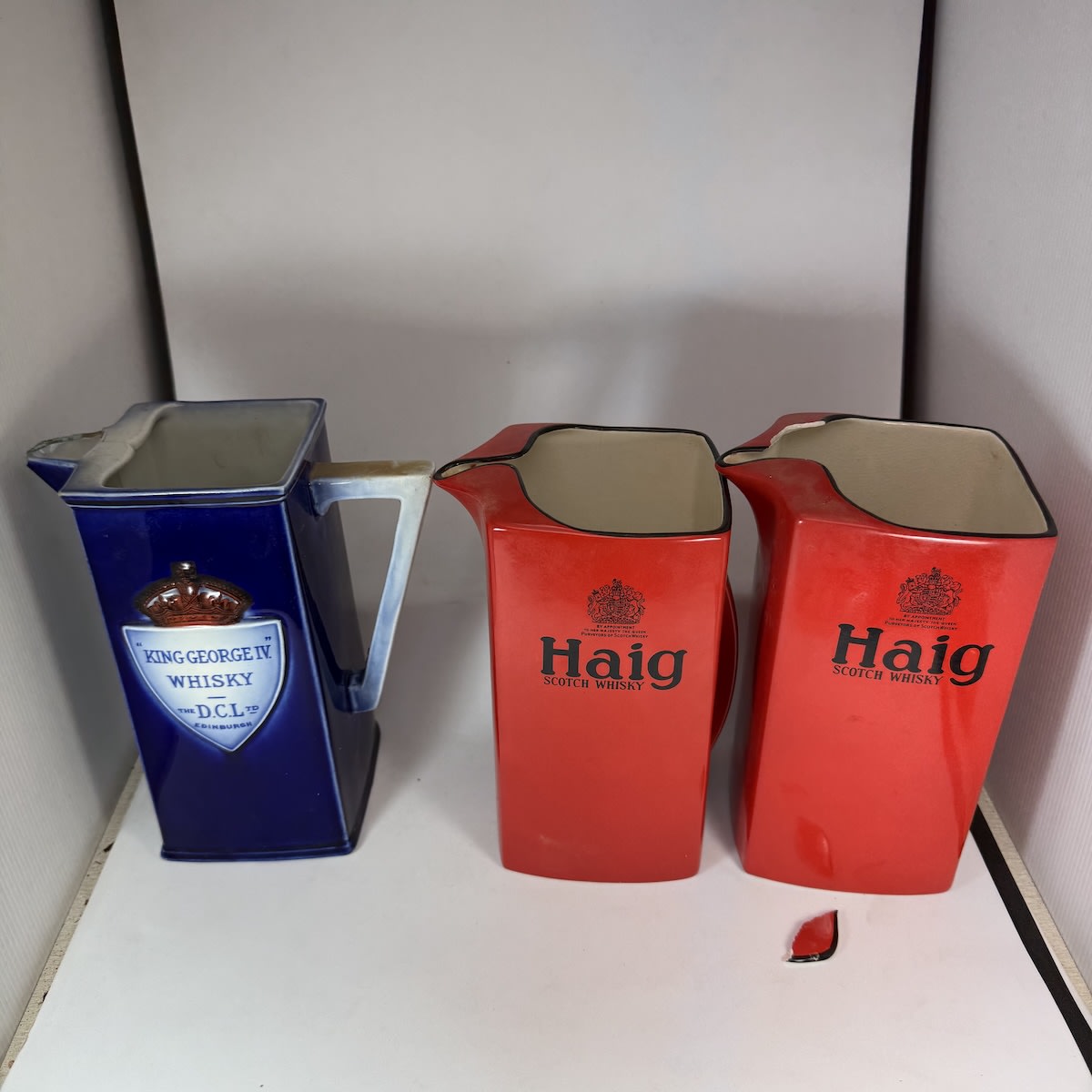 3 Tall Whisky Water Jugs: King George IV Whisky DCL Ltd; 2 x Carlton ware Haig Scotch Whisky red & black jugs.