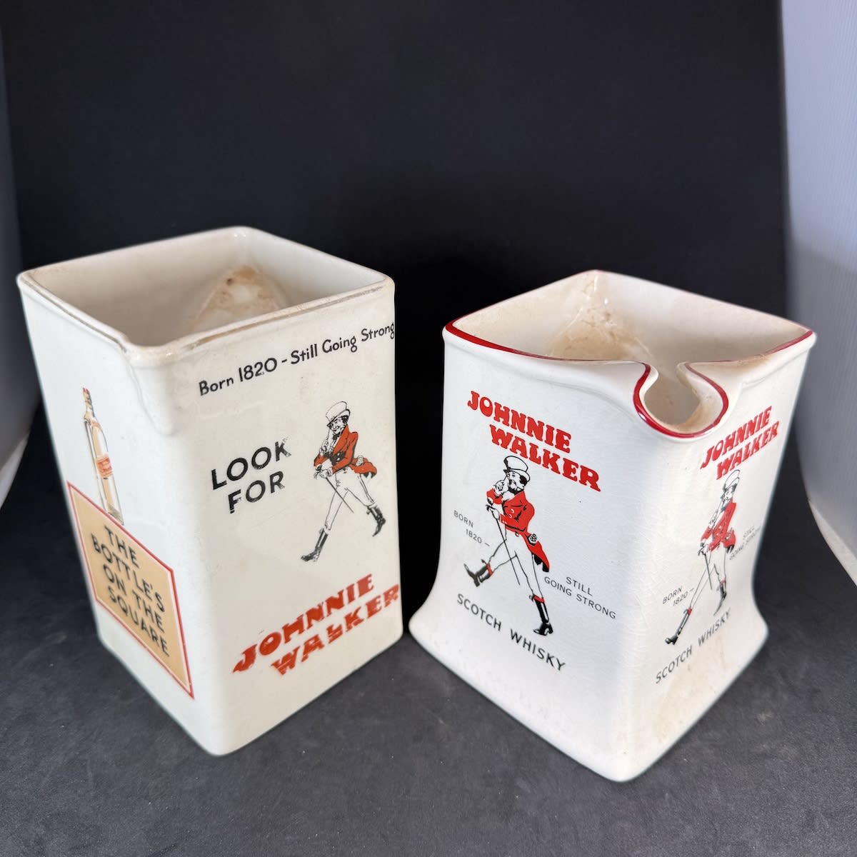 2 Johnnie Walker Whisky Water Jugs: Earlier James Green made with "The Bottle's on the square, The "label" is on the squint."; Wade one with flared out base.