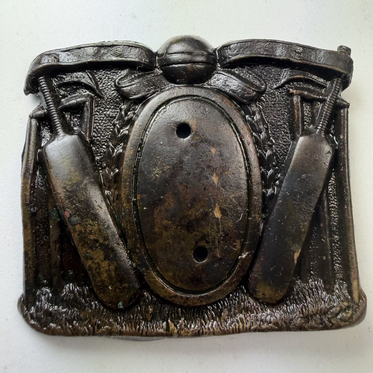 Cricket Belt Buckle / Sash Buckle. Bats leaning on stumps to either side. Ball and banner across the top. Missing a central pinned piece on a plain oval.