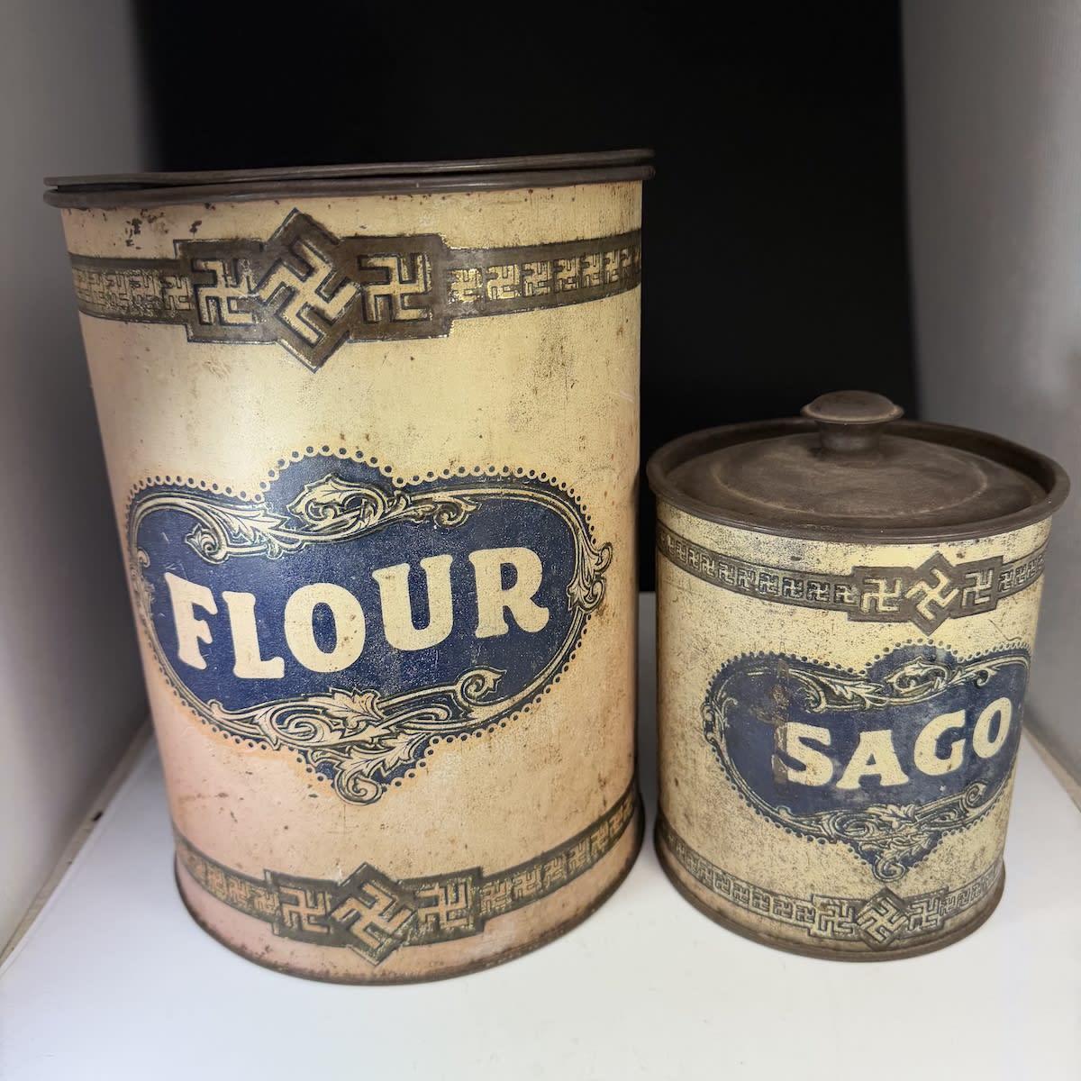 2 Tins. Large Flour tin and small Sago tin. Early Swastika pattern (predating its more infamous use).