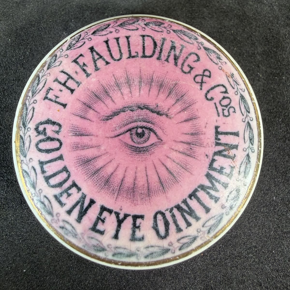 Pot Lid. F. H. Faulding & Cos, Golden Eye Ointment. Black on Pink. Gold Border. 44 mm diameter. (South Australia)