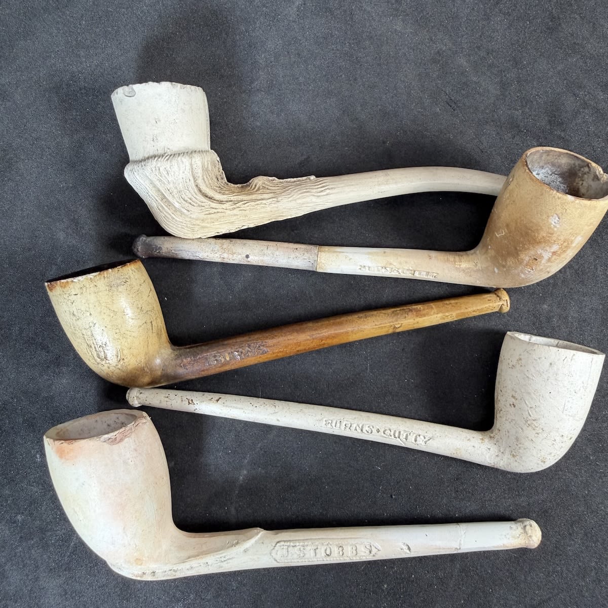 5 Complete Clay Pipes: Stubbs No. Shields; 3 x Burns Cutty different types; Wood grain type finish.