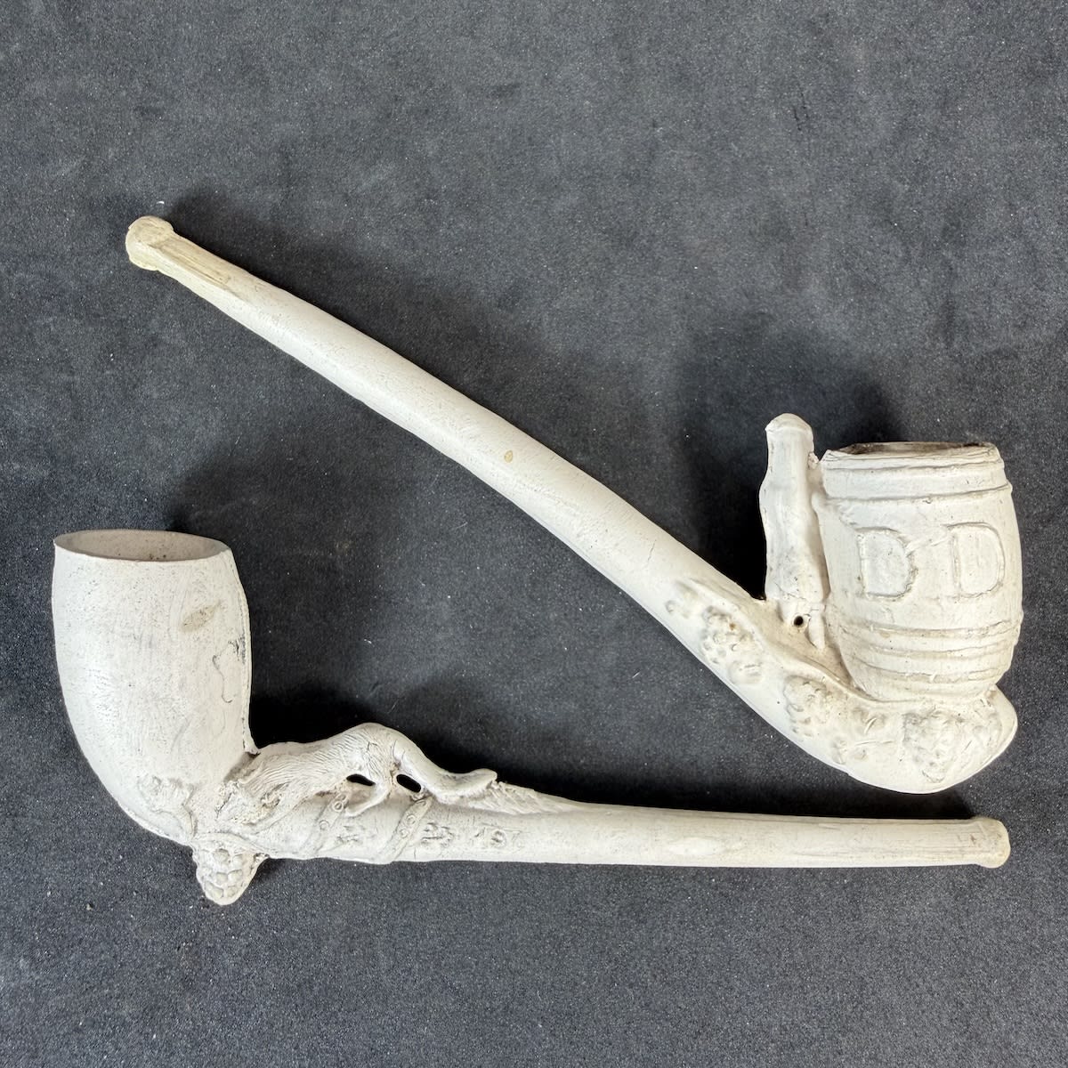 2 Complete Clay Pipes: Small figure with a large barrel that has DD on it; Fox or Dog on the stem with a grape vine and grapes.