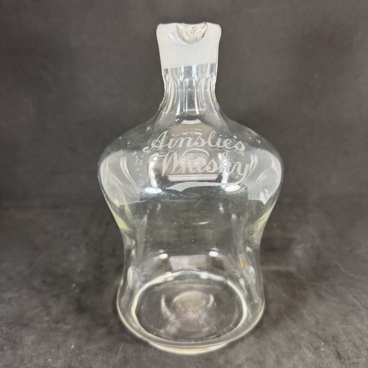 Whisky Decanter. Ainslie's Whisky etched in script on shoulder. Very fine glass. Ground inner neck but no stopper. Polished pontil scar to base.