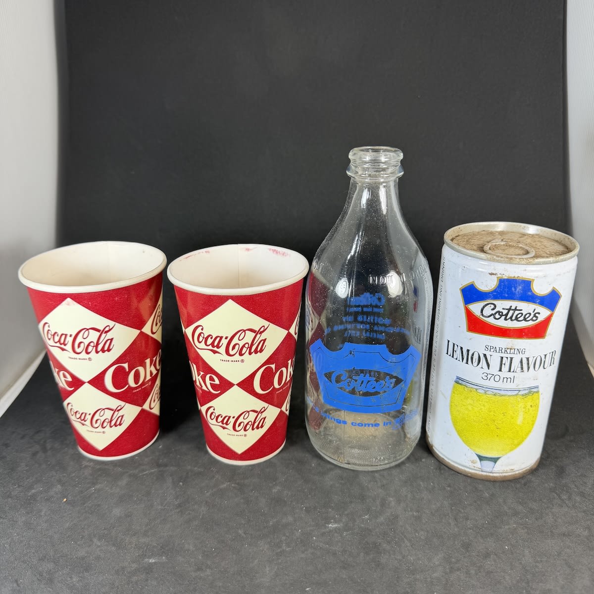 4 Soft Drink Items: 2 x Coca Cola, Coke, Wax Cups; Cottee's Passiona Ceramic Label Crown Seal; Cottee's Lemon Flavour Can.