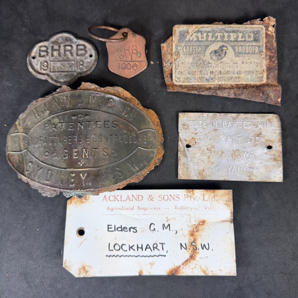 5 metal nameplates etc plus paper tag: BHRB1918 (Broken Hill Road Board?' BRB No 91, 1906; Multiplo Kerosene Brooder; Western Barbed Wire & Nail Pty Ltd; Hannam & Co Sydney; Ackland & Sons Rupanyup, Elders Lockhart.
